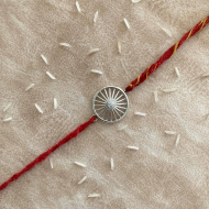 A Silver Wheel Of Progress Rakhi With Red Moli Thread For Bhaiya